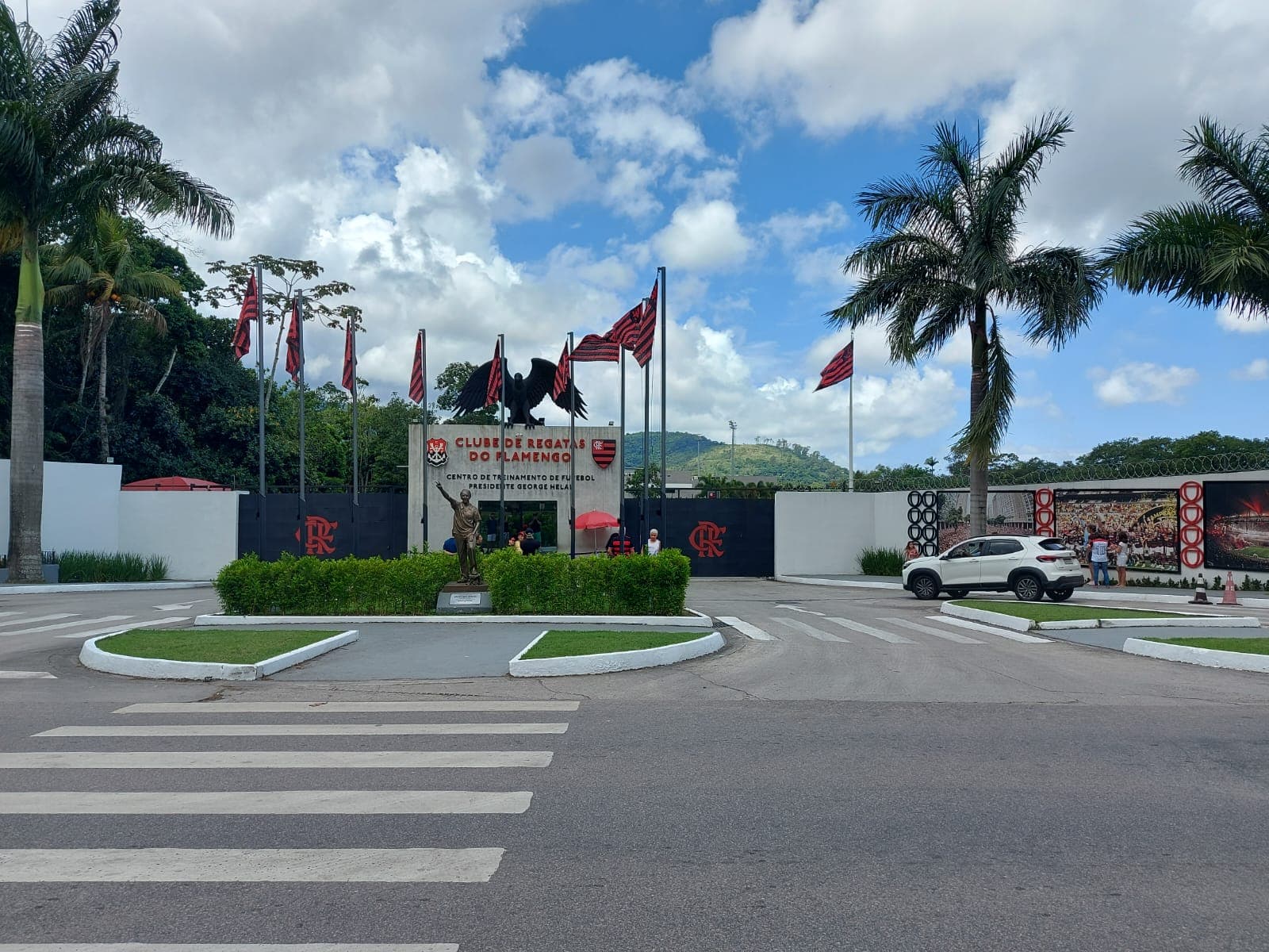 Entrada Ninho do Urubu com identidade visual inaugurada em 2024: bandeiras atrás da estátua de George Helal e fotos na lateral