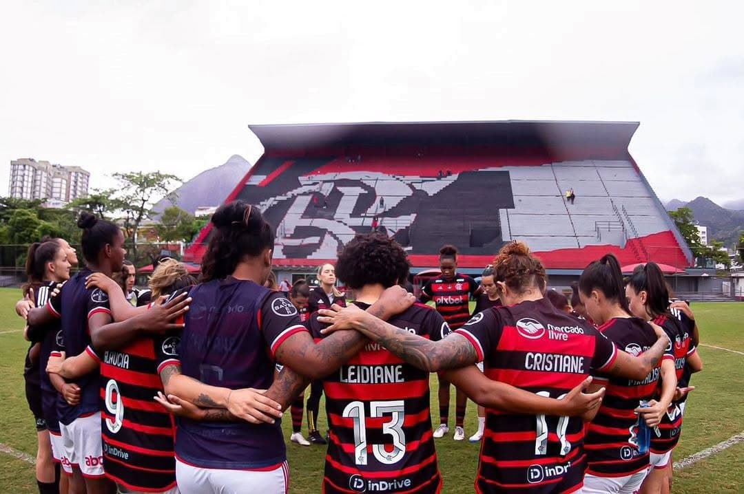 Elenco feminino reunido dentro de campo, na Gávea e a nova arquibancada de fundo