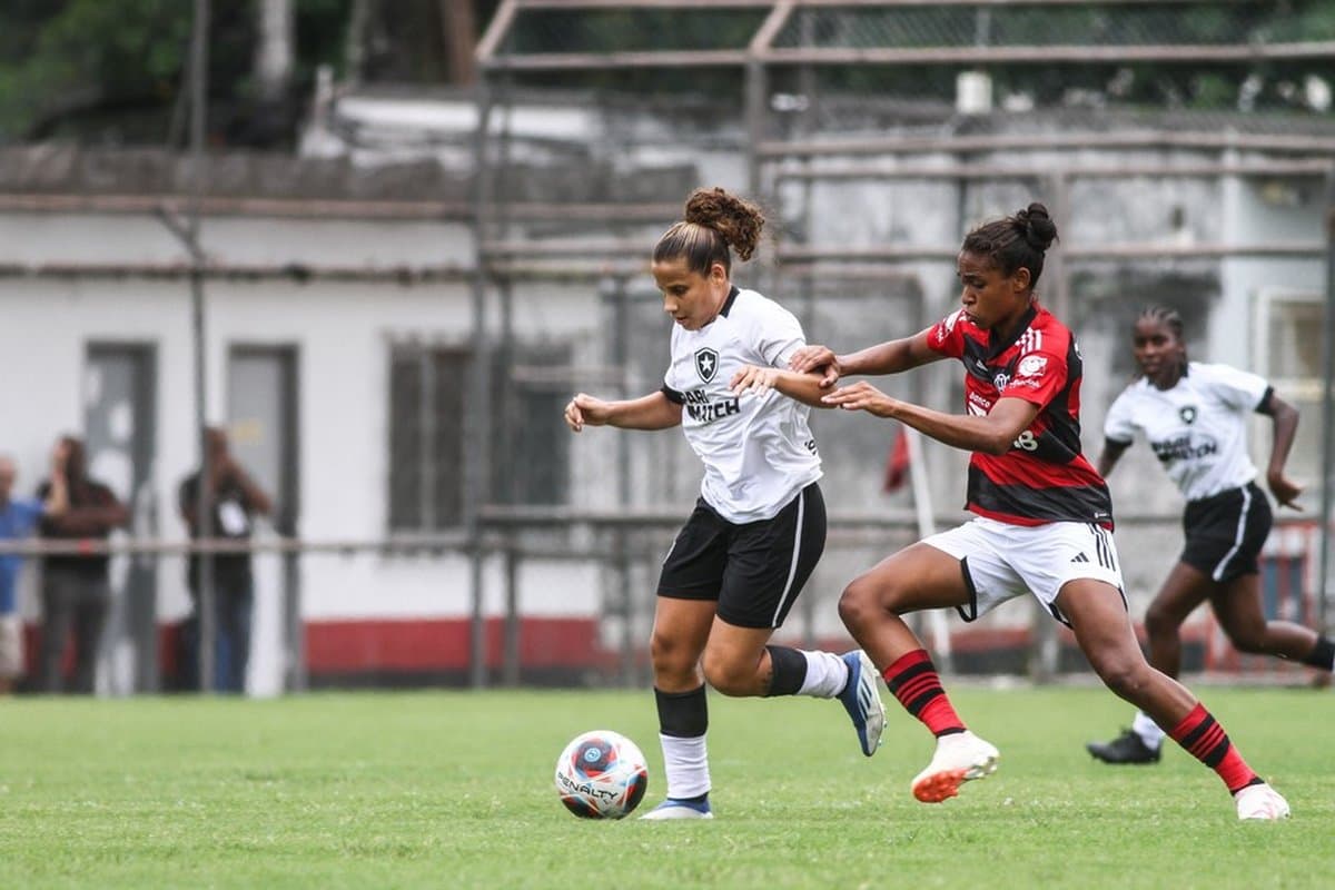 Na foto duas jogadoras disputam a bola, a atleta do Botafogo está mais próxima e a do flamengo vem logo atrás tentando a recuperação