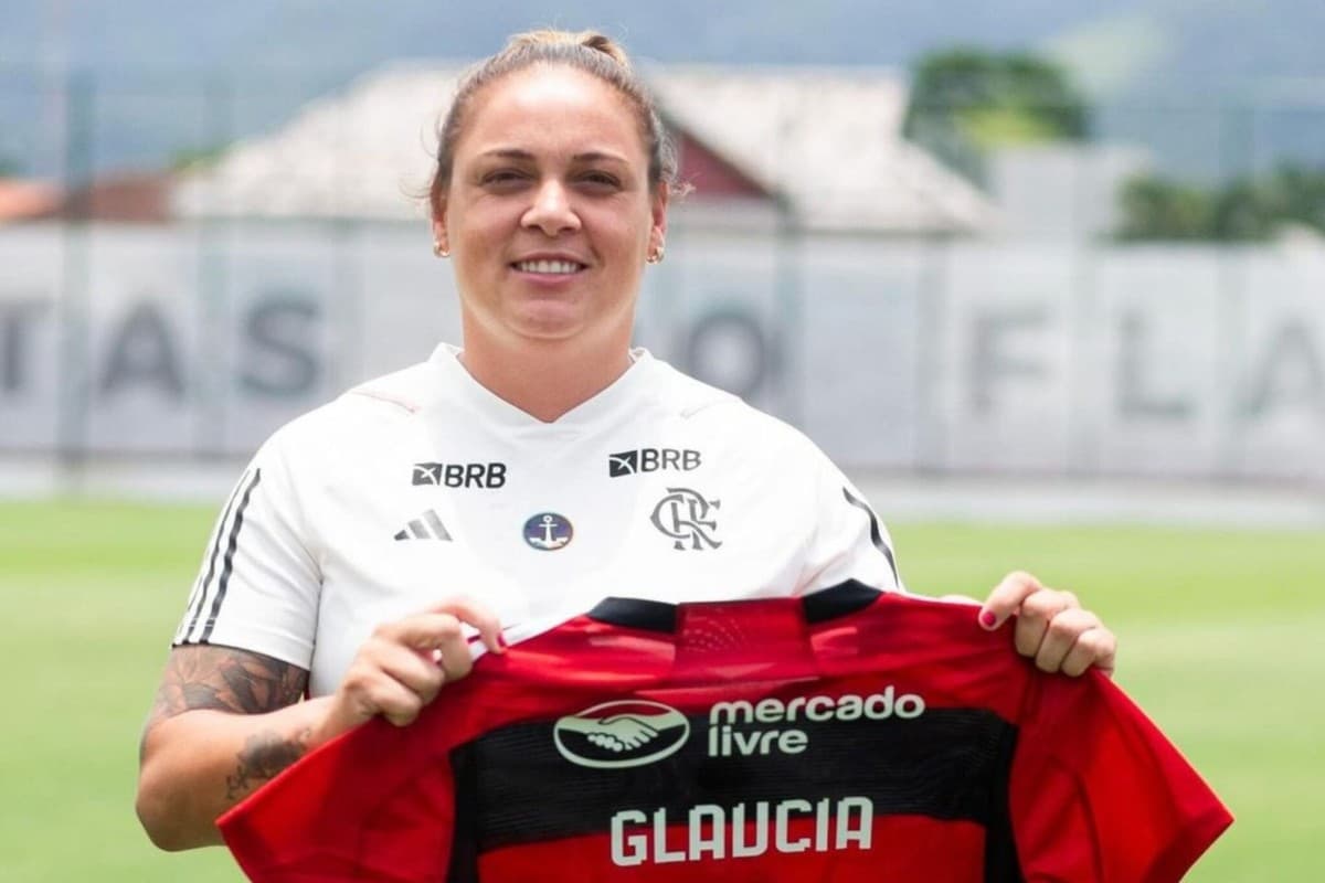 Glaucia está sorrindo e segurando o Manto rubro-negro com seu nome na parte de trás