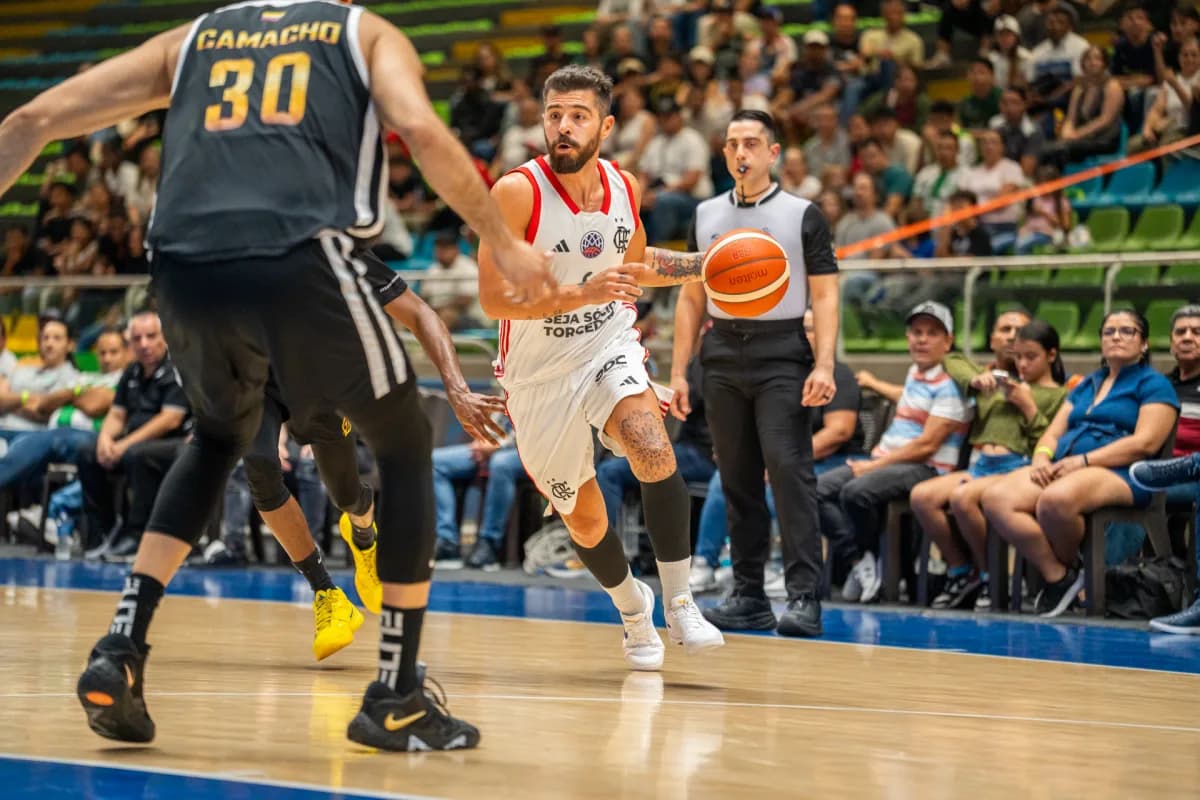 Franco Balbi carrega a bola com a mão esquerda de frente para jogador do Paisas Basketball