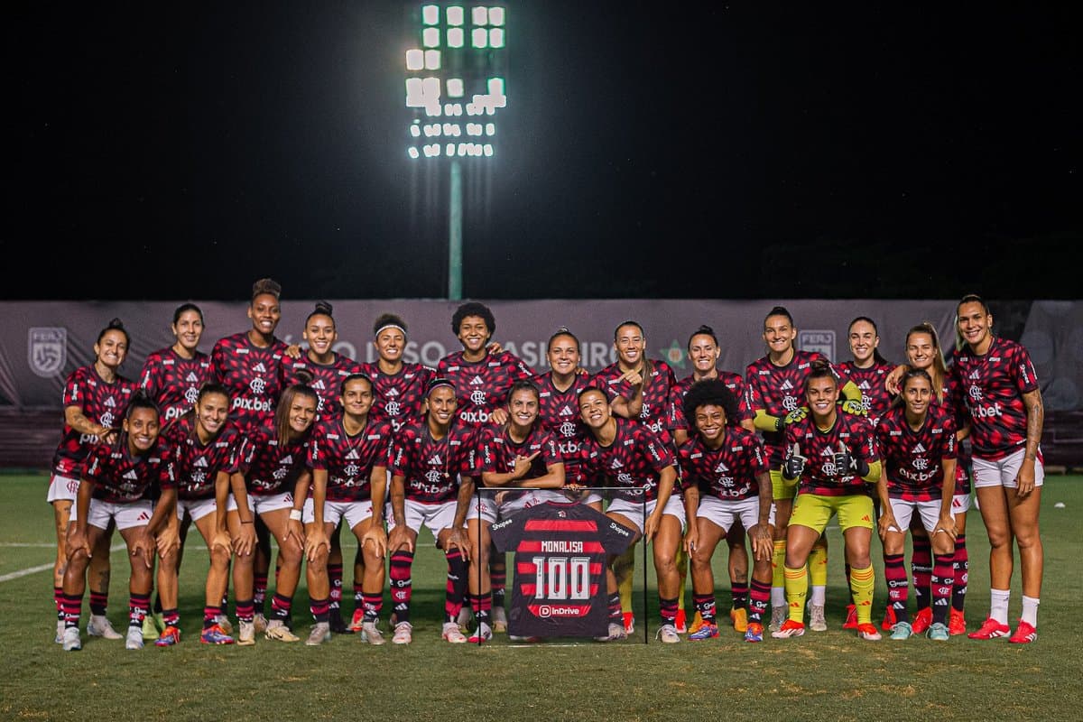 O elenco está posicionado para a tradicional foto antes do jogo e seguram a placa comemorativa da lateral Monalisa que completou 100 jogos disputados com o Manto