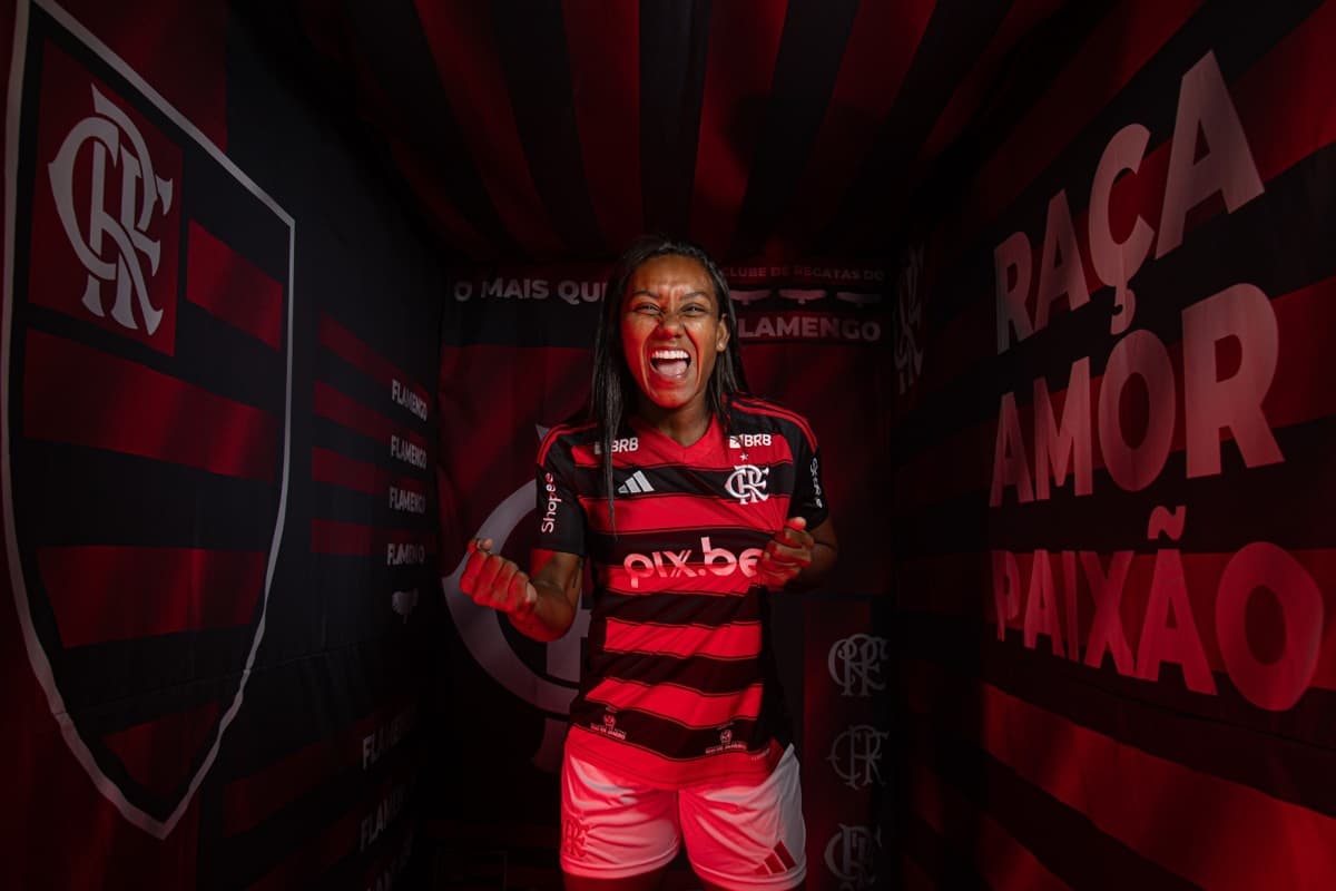 Juliana está em um cenário onde nas paredes tem um escudo grande do Flamengo de um lado e do outro os dizeres: Raça, Amor e Paixão, o cenário é todo vermelho e preto, a atleta está no meio segurando o Manto e mostrando o escudo