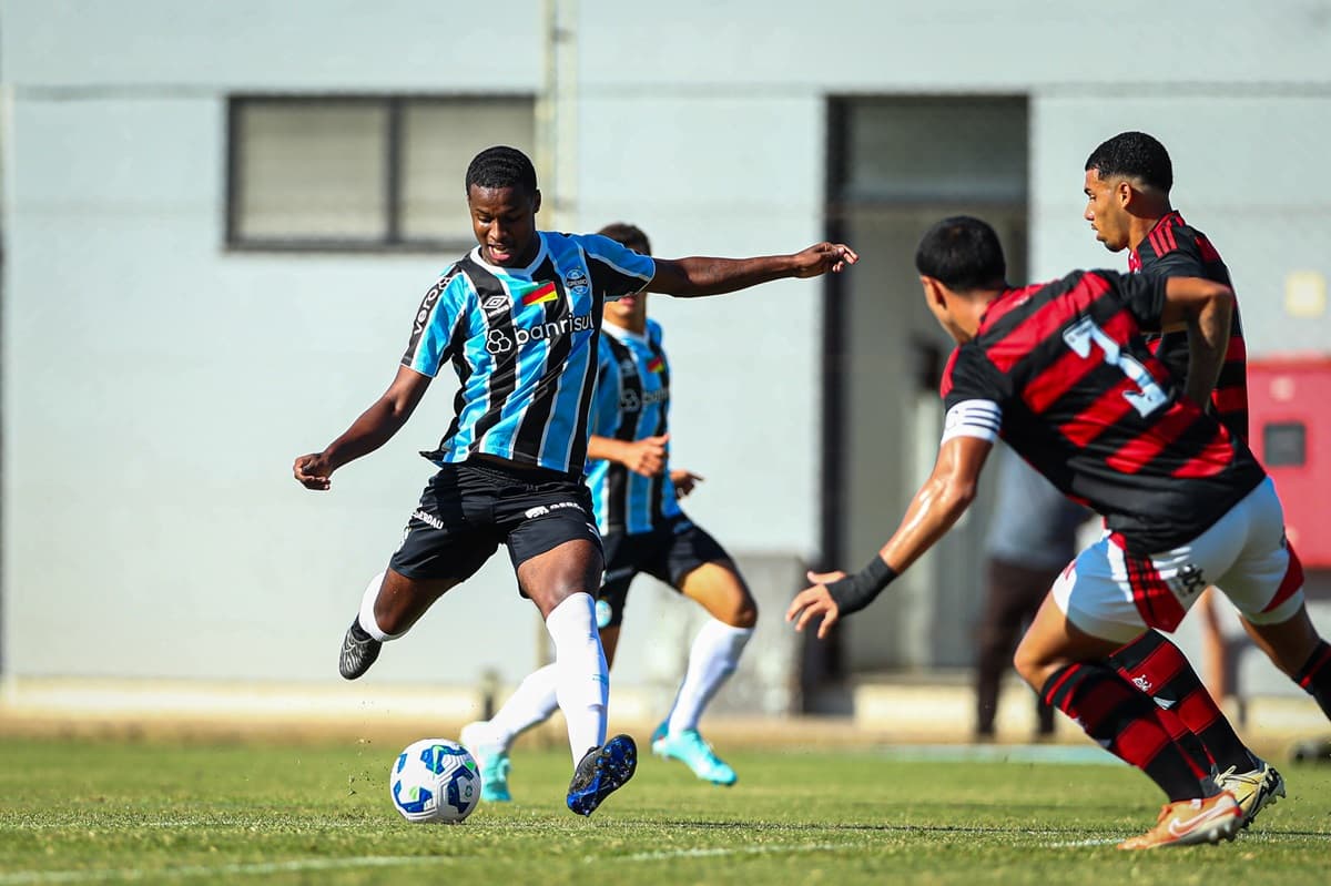 Jogador do Grêmio tenta jogada e é observado por atletas do Flamengo