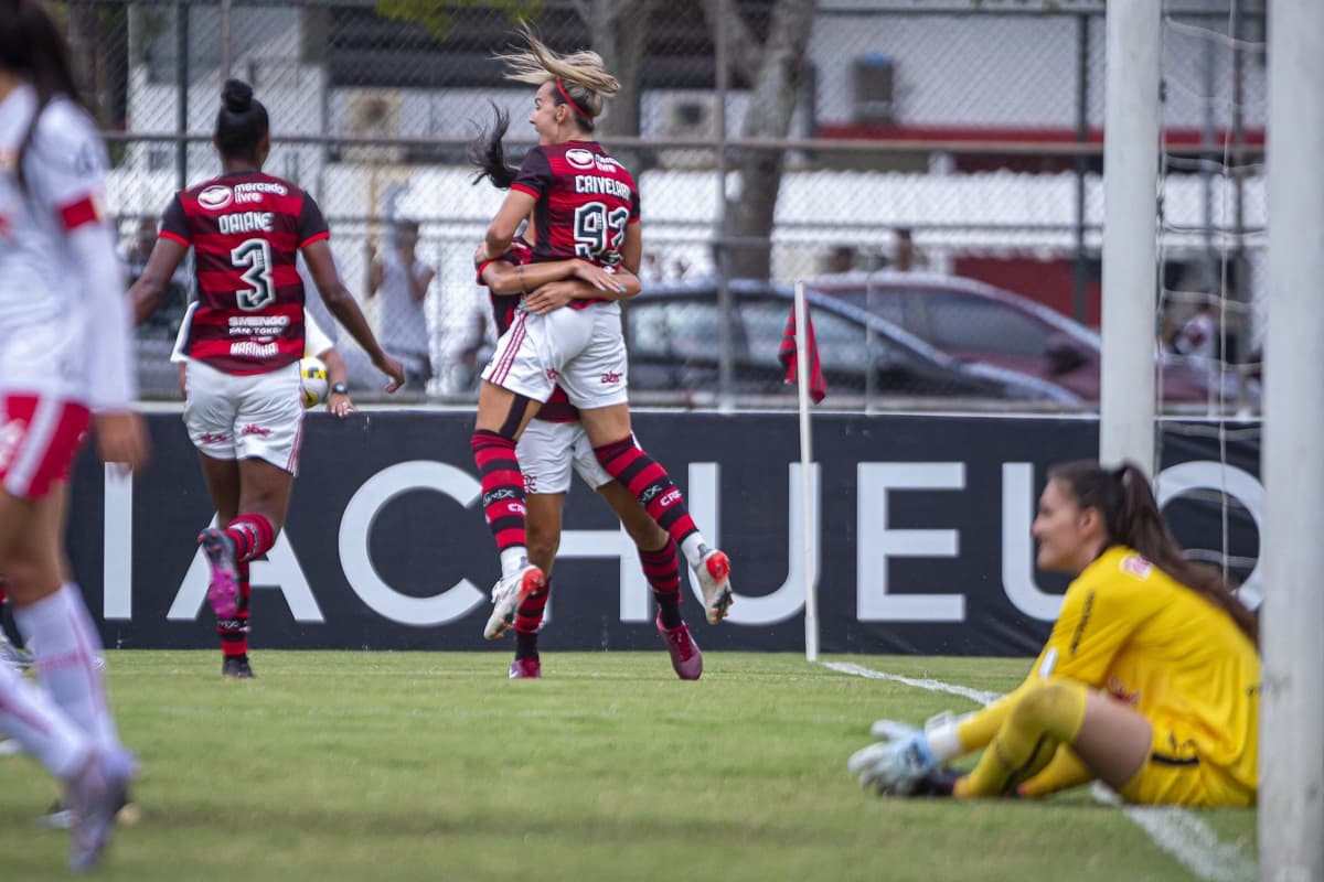 Daiane e Crivelari comemoram o gol, enquanto a goleira Karol está sentada e repreendendo as colegas de time