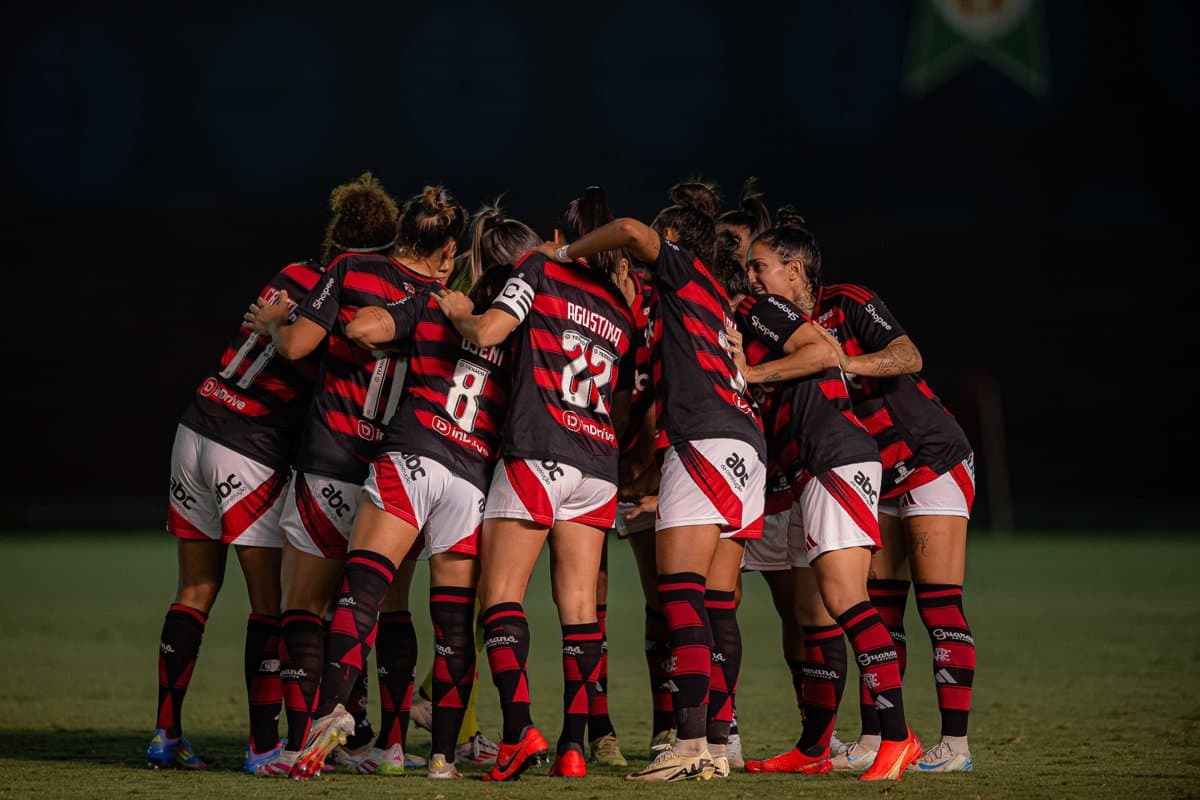 As jogadoras estão reunidas no gramado em uma roda, no momento de concentração