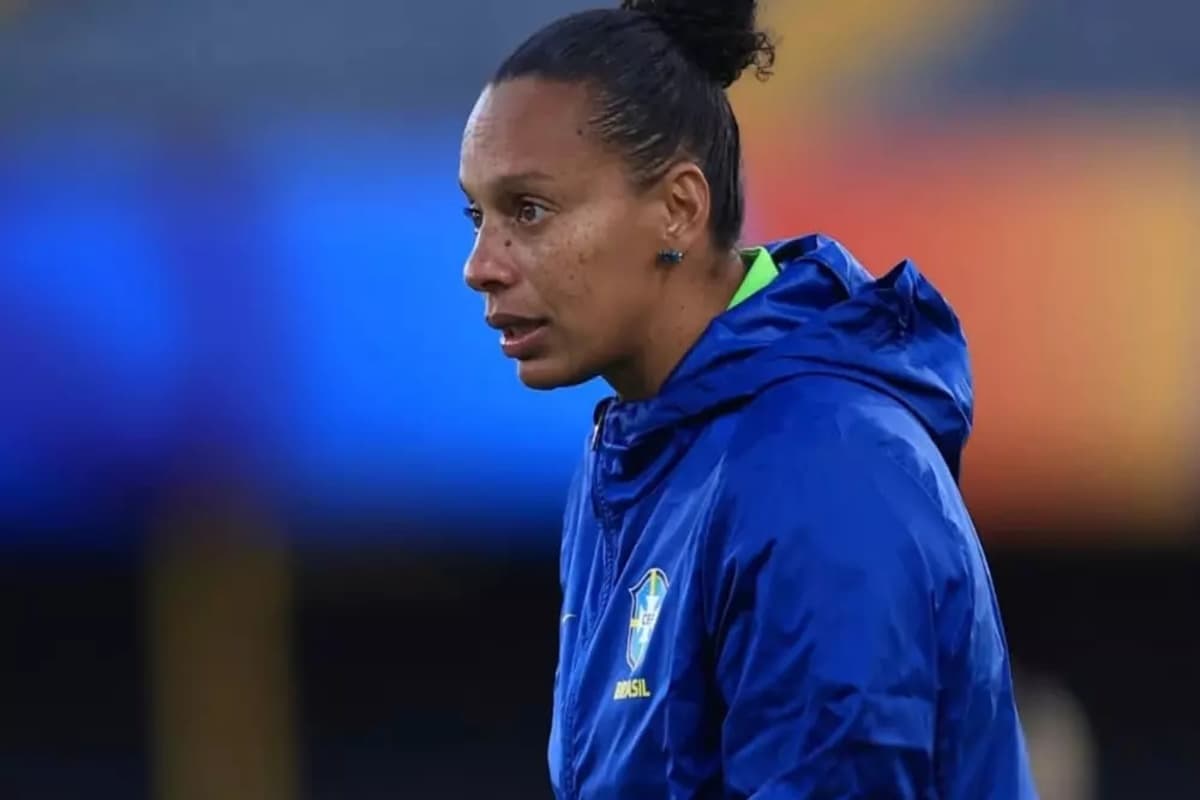 Rosana está de perfil, usando um casaco azul da Seleção Brasileira, cabelo preso e está com a expressão séria