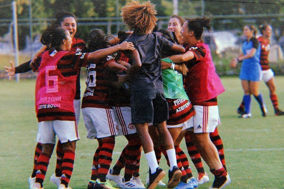As jogadoras reservas do Flamengo estão usando coletes e abraçando as titulares que venceram o Botafogo por 7 a 2 no Cefan