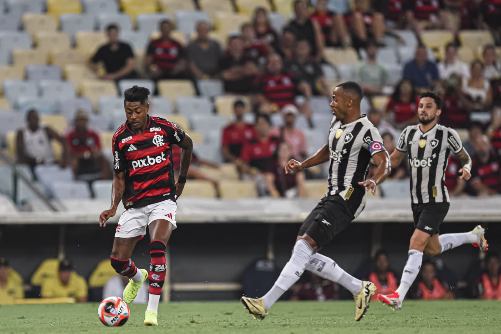 Bruno Henrique cruza enquanto é observado por Marlon Freitas e Alex Telles