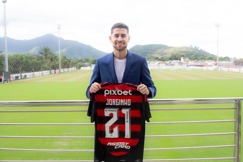 Jorginho segura a camisa 21 do Flamengo; campos do Ninho do Urubu ao fundo