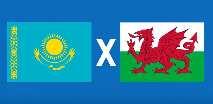 Bandeiras de Cazaquistão e País de Gales lado a lado, separadas pela letra X em fundo azul, representando o confronto pelas Eliminatórias da Europa