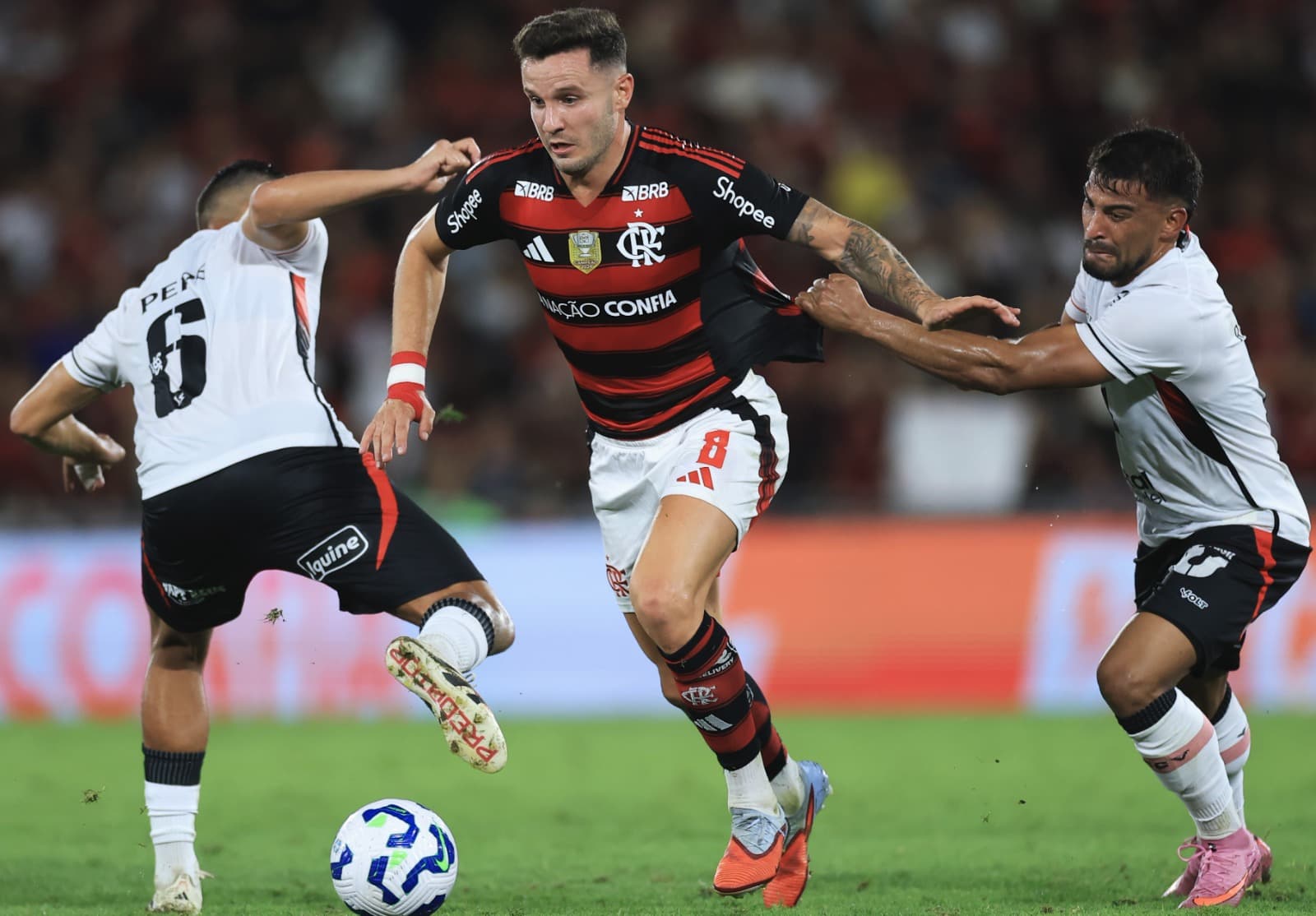 Saúl passa entre dois marcadores do Vitória. Um deles, puxa sua camisa com força