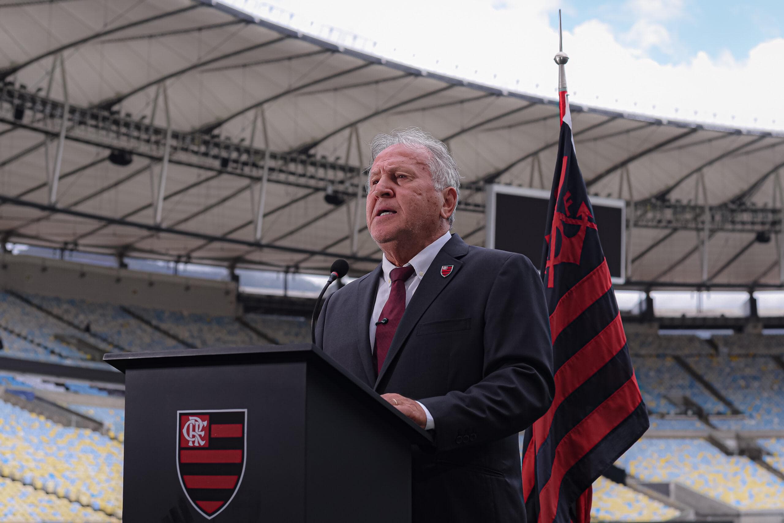 Zico no púlpito com o escudo do Flamengo, ao lado de bandeira do clube, fazendo o papel de chefe de estado para solicitar o reconhecimento da Nação Rubro-Negra na ONU