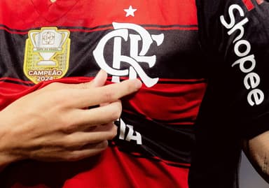 Arrascaeta destaca o escudo do Flamengo ao comemorar um gol; imagem mostra dedos do meia se aproximando do escudo