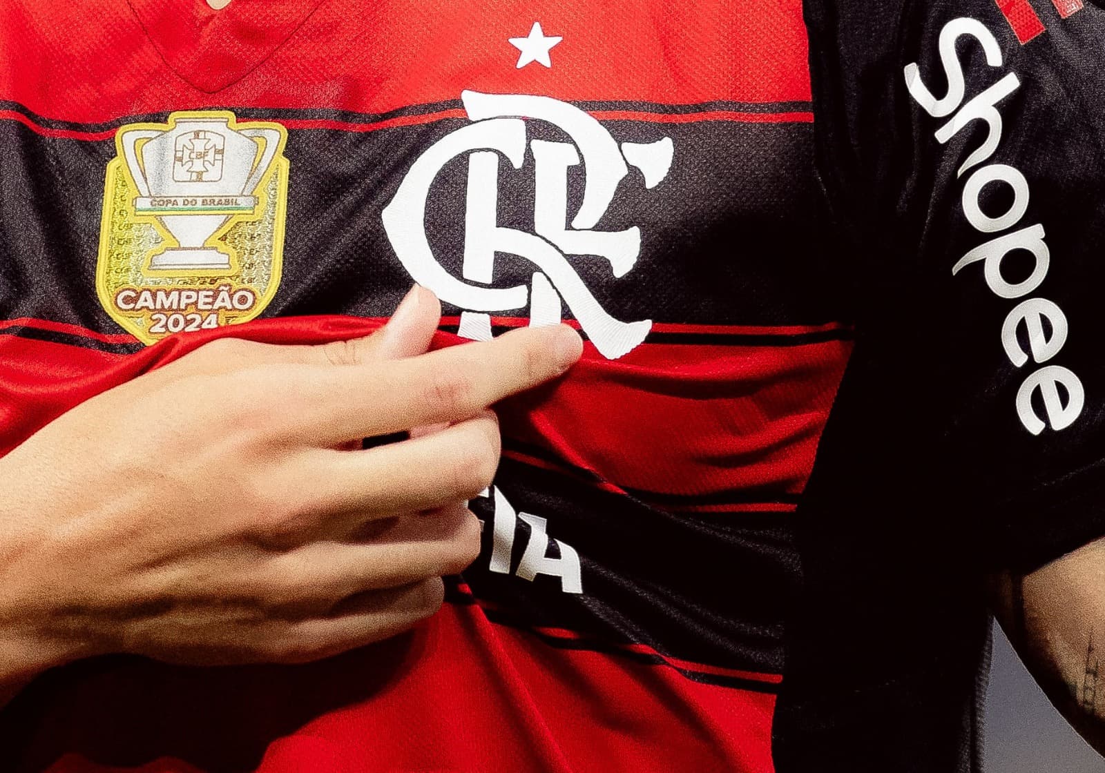 Arrascaeta destaca o escudo do Flamengo ao comemorar um gol; imagem mostra dedos do meia se aproximando do escudo