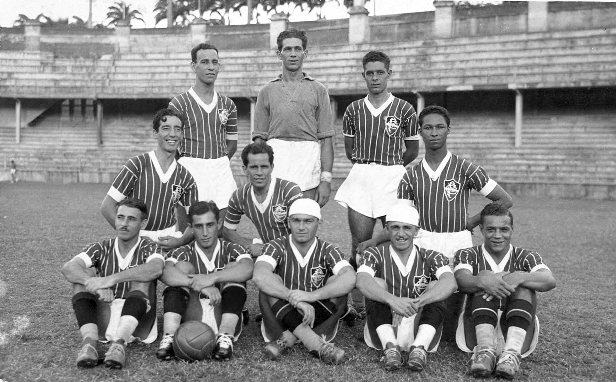 Foto histórica do time do Fluminense em 1936, com jogadores posando no estádio, representando a tradição e as rivalidades clássicas do futebol carioca.