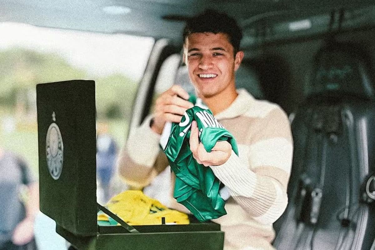 O piloto de Fórmula 1 Lando Norris sorri ao receber uma caixa com duas camisas do Palmeiras, uma na cor verde e outra na cor amarela