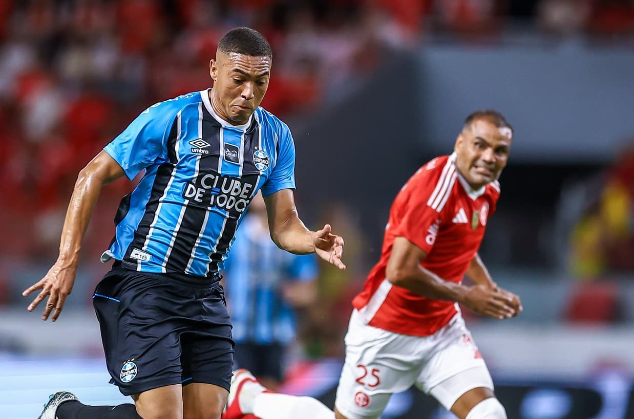 Carlos Vinícius conduz bola perseguido por Gabriel Mercado, que faz careta, em Internacional x Grêmio pelo Gauchão 2026
