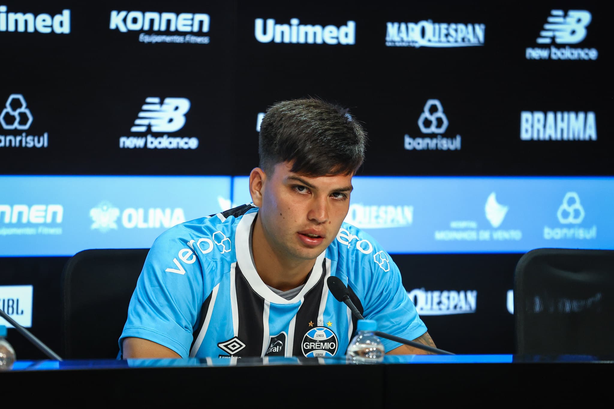 Leonel Pérez fala ao microfone com semblante sério durante coletiva de apresentação no Grêmio