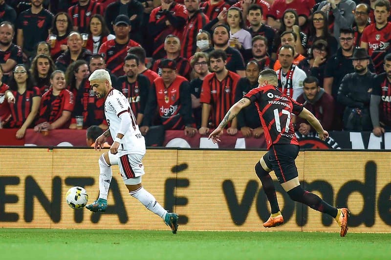 Arrascaeta, do Flamengo, carrega a bola sob olhares de torcedores do Athletico-PR; clubes se enfrentam pelo Brasileirão