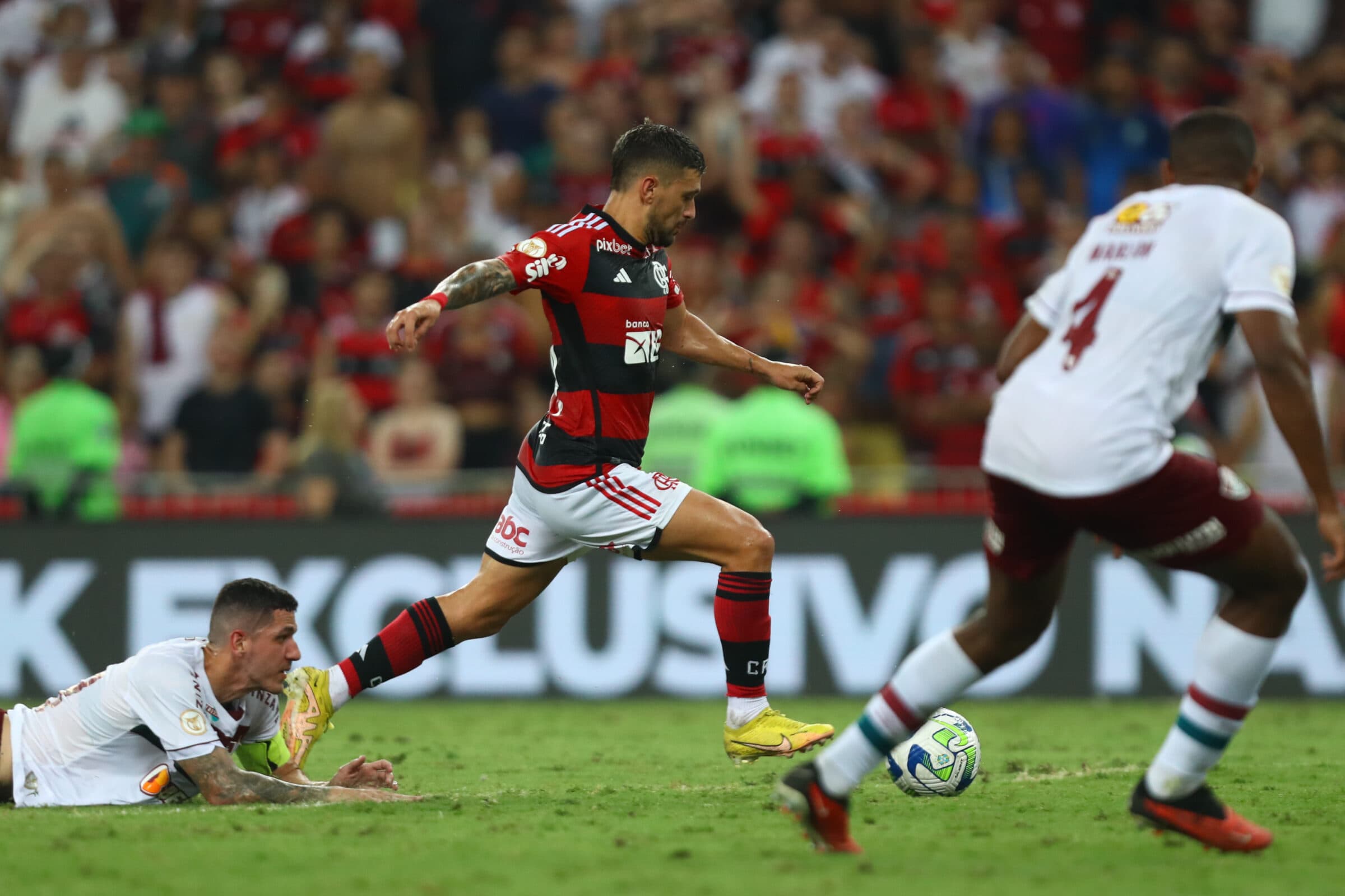 Arrascaeta chuta para o gol enquanto Nino observa do chão após ser driblado no Fla x Flu