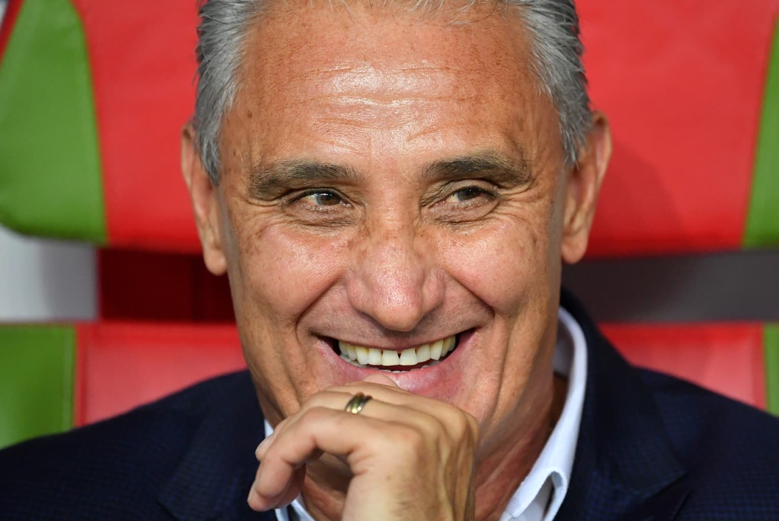 Tite sorri no banco de reservas com a mão no queixo