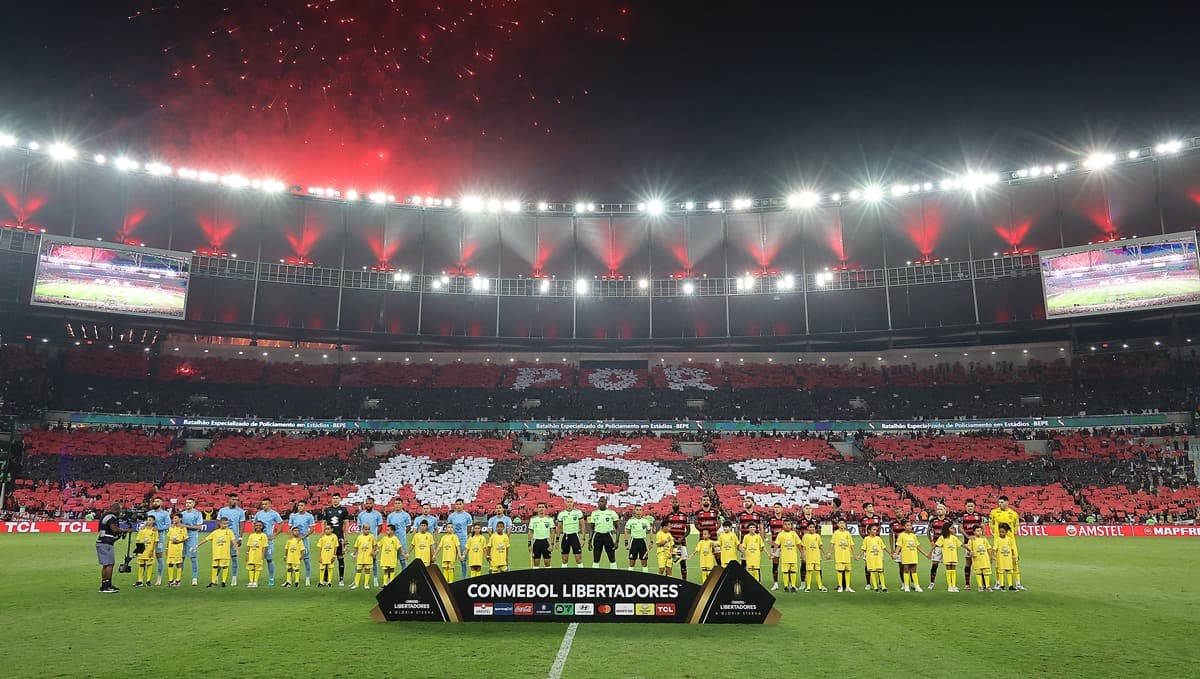 Times de Flamengo e Bolívar perfilados atrás de banner da Copa Libertadores; ao fundo, mosaico da torcida formando "Por nós"