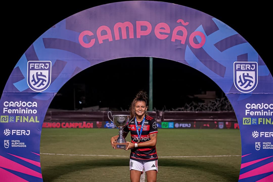 Atacante Laysa levantando a taça do Carioca feminino, ela está com a medalha pendurada no pescoço e segurando o troféu com as duas mãos.