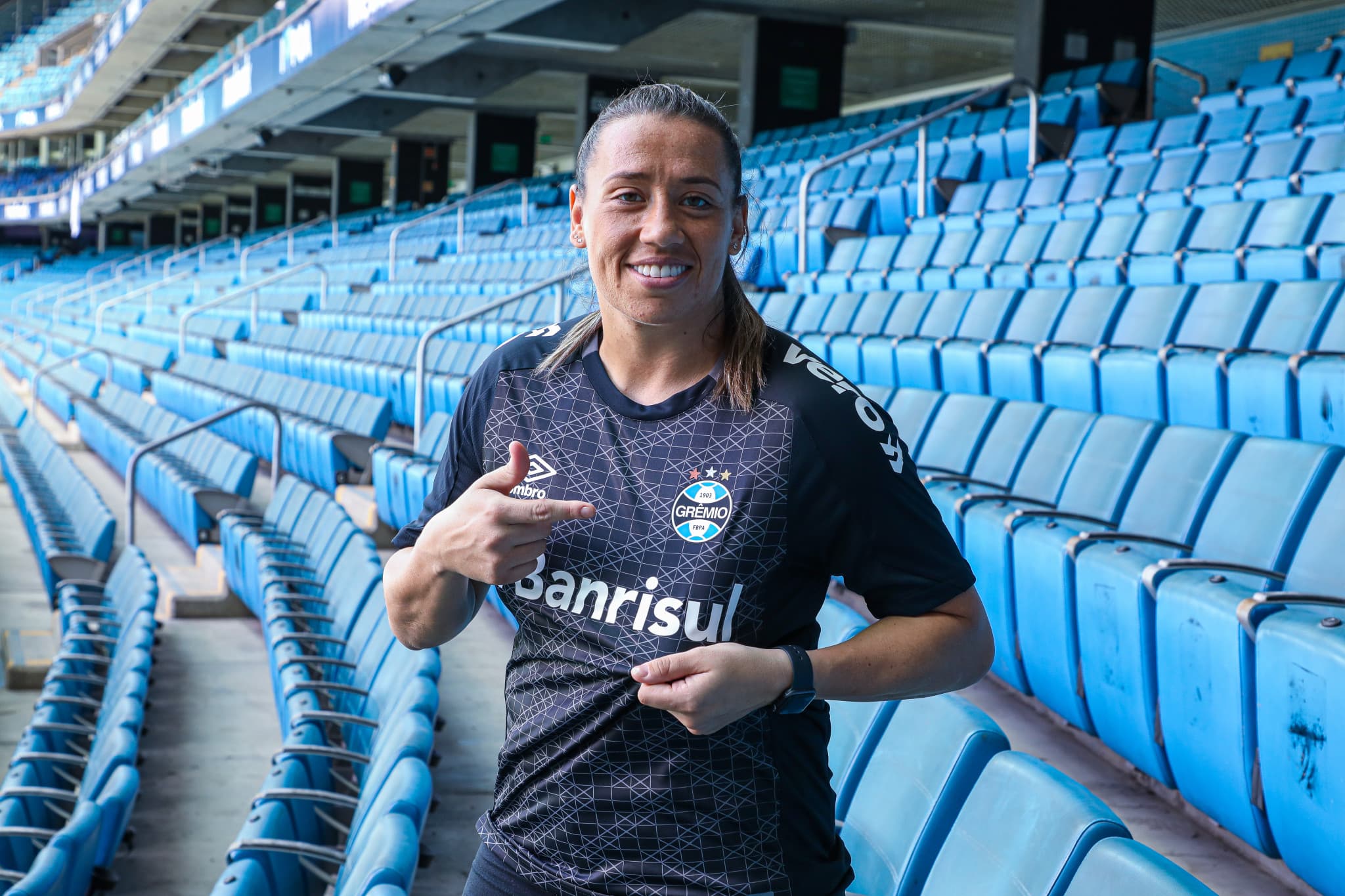 A goleira está sorrindo e apontando para a própria camisa, mostrando o escudo do Grêmio seu clube até dezembro de 2024
