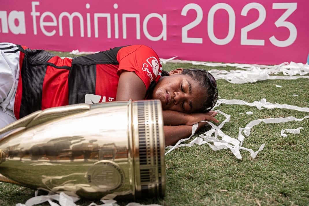 Kaylaine está deitada no gramado ao lado da taça da Copinha