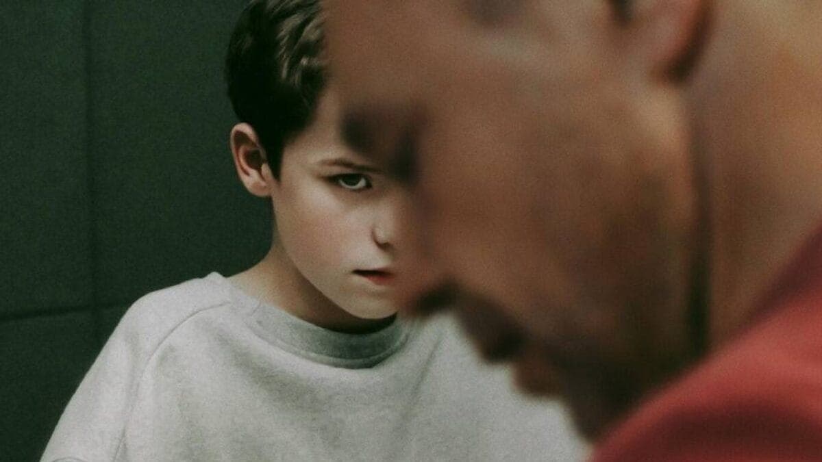 Personagem adolescente que cometeu feminicídio na série Adolescência observa o pai durante depoimento na prisão