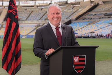 Zico no púlpito com o escudo do Flamengo, ao lado de bandeira do clube, fazendo o papel de chefe de estado para solicitar o reconhecimento da Nação Rubro-Negra na ONU