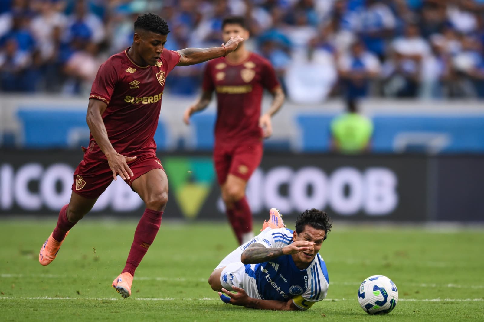 Hércules prepara chute, enquanto Lucas Romero observa caído no chão, em Cruzeiro x Fluminense