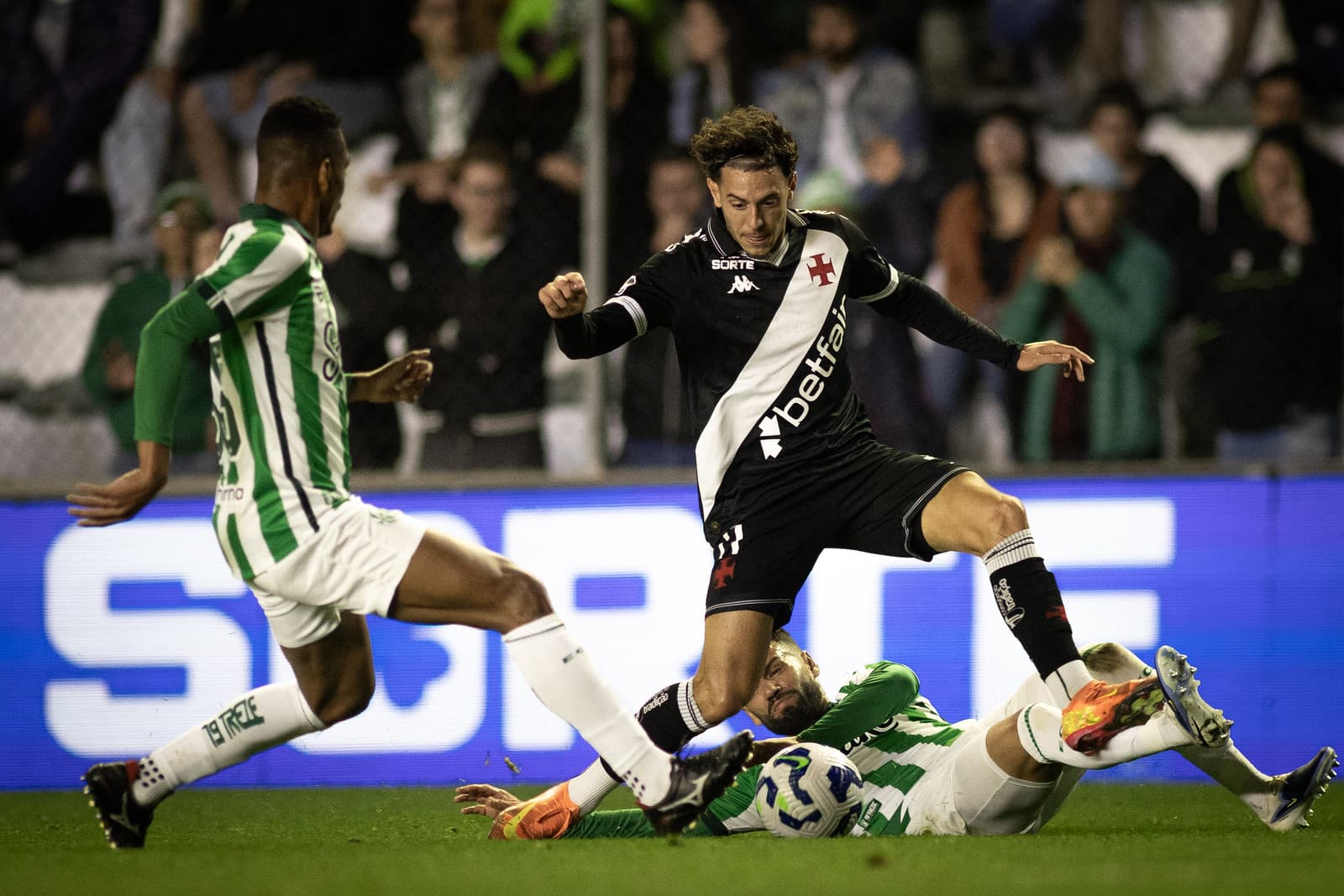 Nuno Moreira, do Vasco, foge de marcação dupla enquanto um jogador do Juventude dá carrinho e outro chega na cobertura durante duelo no Alfredo Jaconi pelo Brasileirão 2025