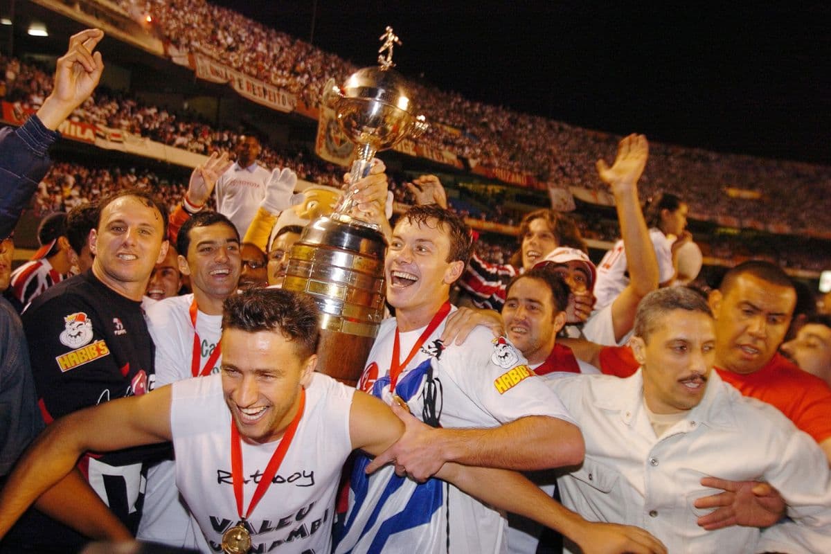 Jogadores do São Paulo comemoram o título da Libertadores 2005 no Morumbi. Atletas como Rogério Ceni, Lugano e Danilo estão ao lado da taça celebrando a conquista.