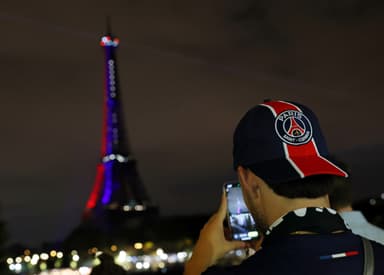 Torcedor do PSG com boné do clube tirando foto da famosa torre Eiffel em Paris