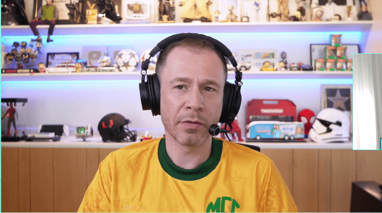 Tiago Leifert aparece em seu estúdio durante uma live, usando fone com microfone e camisa amarela, enquanto comenta temas do futebol brasileiro.