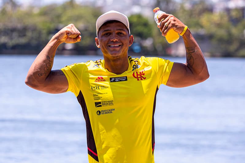 Isaquias Queiroz, canoísta brasileiro, veste camisa do Flamengo e sorri enquanto levanta os braços às margens da Lagoa Rodrigo de Freitas, em imagem relacionada ao Flamengo e ao esporte olímpico.