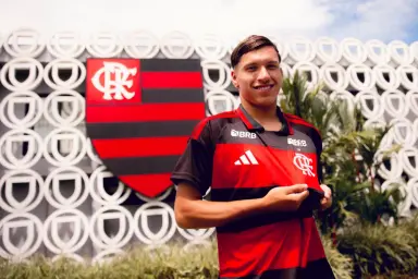 Juan Sayago posa com a camisa Flamengo em frente ao módulo da base no Ninho do Urubu