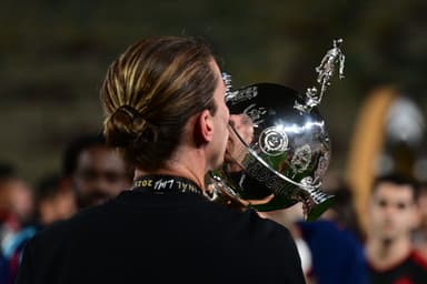 Filipe Luís, de costas, beijando o troféu da Copa Conmebol Libertadores durante a celebração do título de 2025. Ele usa a medalha da final de Lima no pescoço.